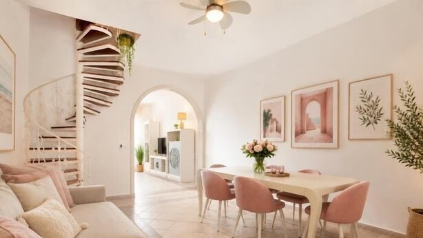 Una sala de estar moderna con un sofá, una mesa de comedor con sillas, una escalera en espiral y cuadros en la pared.