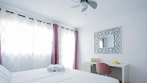 Una habitación de hotel con cama, escritorio, silla, ventilador de techo y un espejo decorativo.