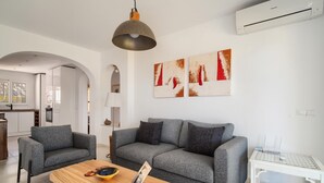 Una sala de estar moderna con un sofá gris, una mesa de centro de madera y una mesita auxiliar blanca.