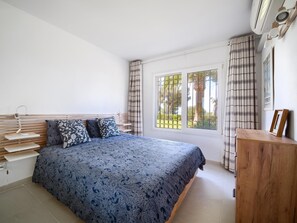 Une chambre à coucher avec un lit, une table de chevet, une commode en bois et une fenêtre avec des rideaux.