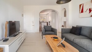 Una sala de estar moderna con un sofá gris, una mesa de centro de madera y un televisor sobre un mueble blanco.
