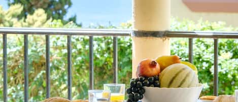A breakfast setup on a balcony with a view of the sea, including fruits, pastries, and glasses of orange juice.