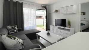 En moderne stue med sofa, sofabord og fjernsyn. Der er en skydedør, der fører til et udendørs område.