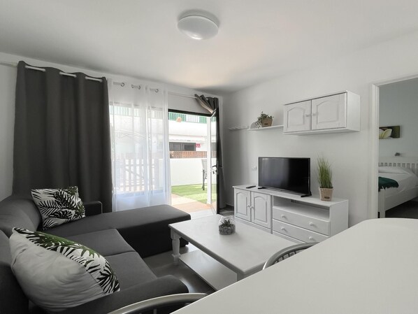 A modern living room with a sofa, a coffee table, and a TV. There is a sliding glass door leading to an outdoor area.