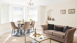 Een woonkamer met een ronde tafel, stoelen, een bank en een kroonluchter.