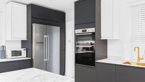 Een moderne keuken met een roestvrijstalen koelkast, een ingebouwde magnetron, oven en een gouden kraan.