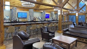 A bar area with multiple seating options, including leather sofas and bar stools, a television mounted on the wall, and a stone pillar.