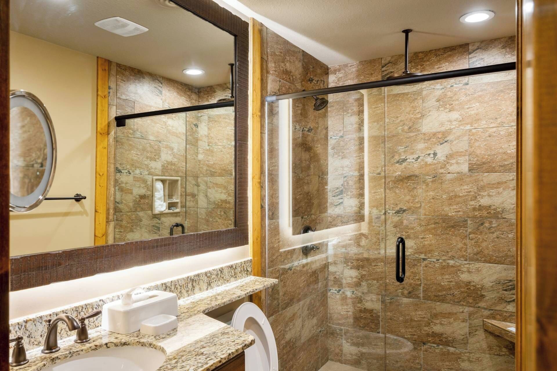 A modern bathroom with a glass-enclosed shower, a marble countertop, and a large mirror.
