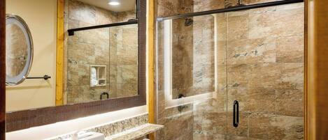 A modern bathroom with a glass-enclosed shower, a marble countertop, and a large mirror.