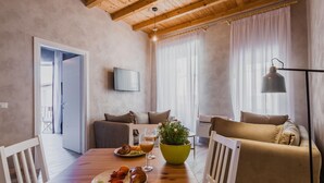 Een gezellige woonkamer met een houten plafond, een flatscreen televisie aan de muur, een eettafel met borden eten, en een bank met kussens.