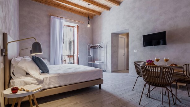 Een slaapkamer met een bed, nachtkastje, lamp en een zithoek met stoelen en een tafel.