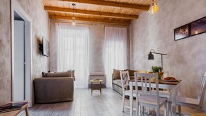 Een gezellige woonkamer met een bank, een eettafel met stoelen en een kleine bijzettafel met een lamp.