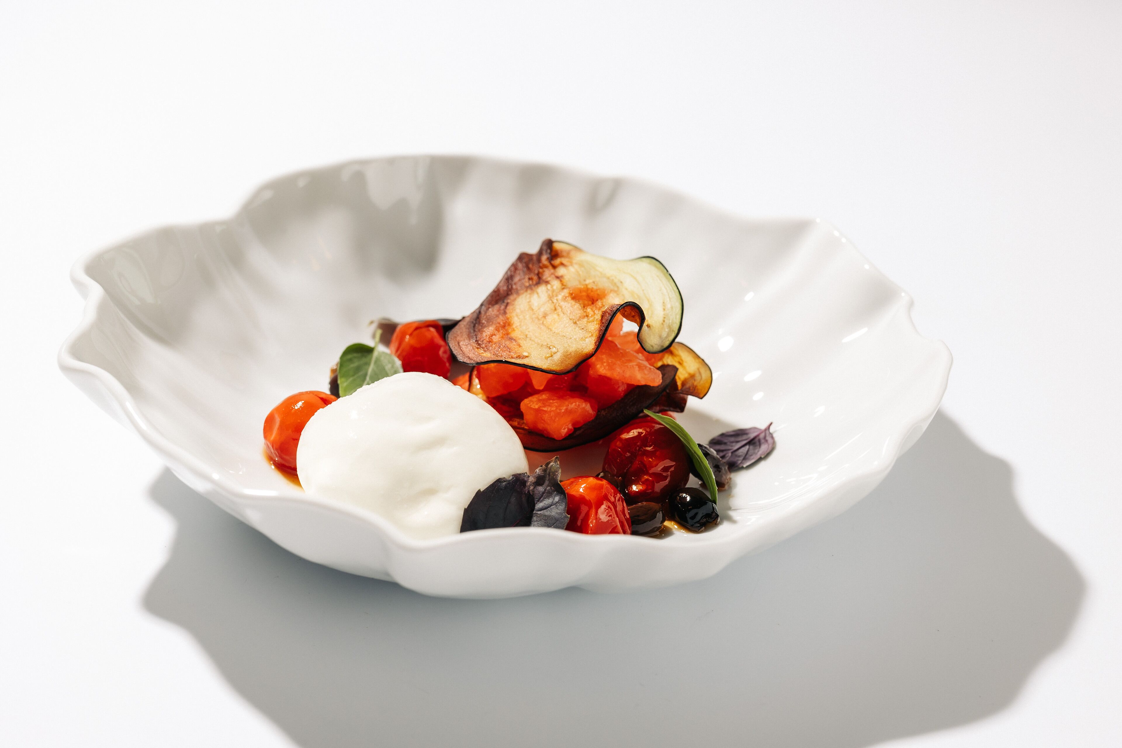 A white plate with a dish containing a grilled vegetable, possibly zucchini, and a dollop of cream or sauce.