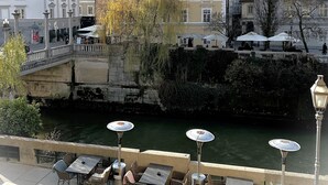 A riverside view with buildings, a bridge, and outdoor seating by the water.