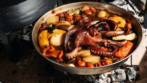 A pan with octopus and vegetables over an open fire.
