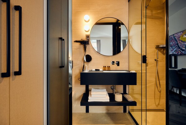 A modern bathroom with a black sink, a round mirror, and a glass shower enclosure.