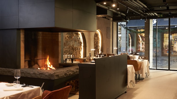 A restaurant interior with a stone fireplace, tables set for dining, and a view of the street outside.
