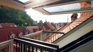 A view from a balcony with a skylight, overlooking a densely packed urban area with traditional red-roofed buildings and a church spire in the distance.