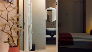 A modern hotel room with a bed, a bathroom with a sink and mirror, and a vase with flowers.