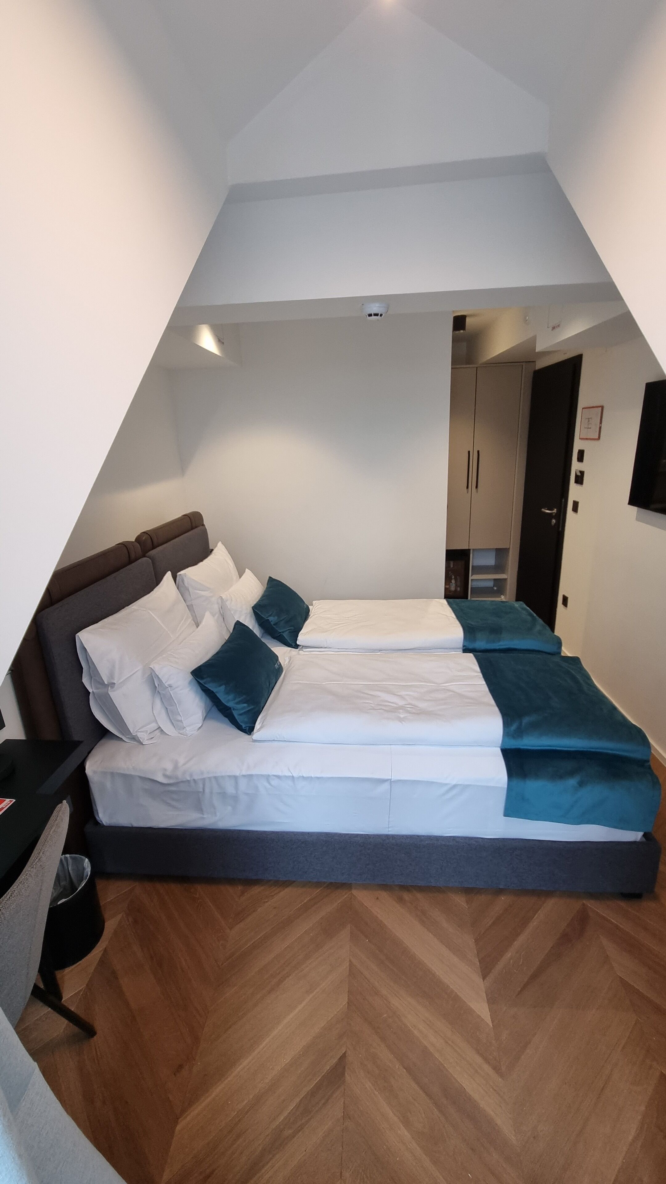 A triangular room with a bed, a desk, and a wardrobe.