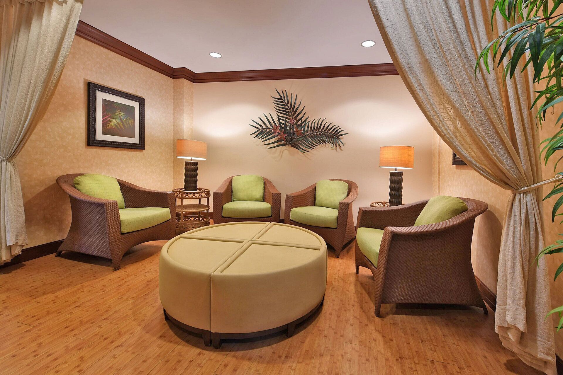 A room with wicker chairs, a round ottoman, and a wall-mounted decorative piece.