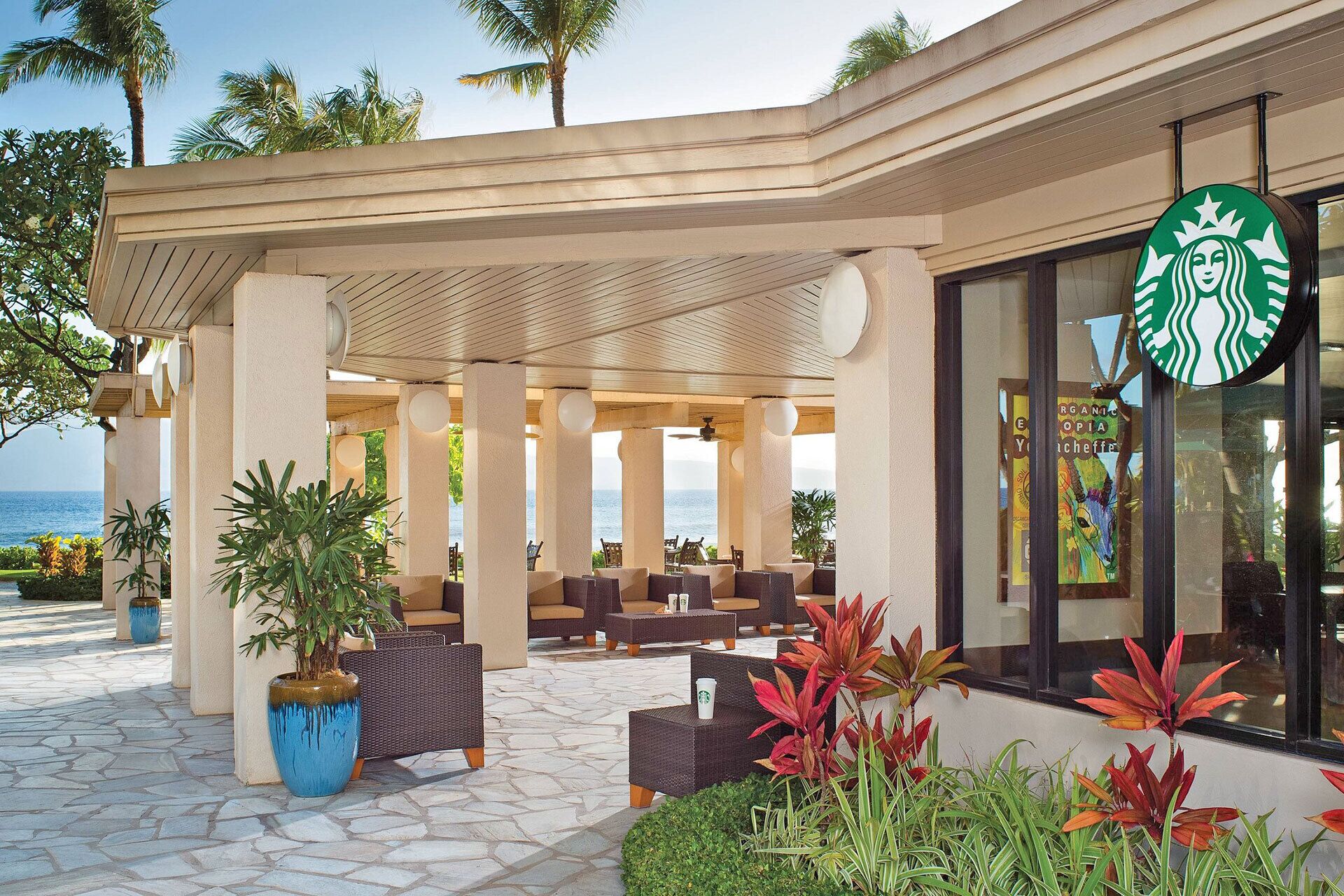 A covered outdoor seating area with a view of the ocean, featuring a Starbucks sign.