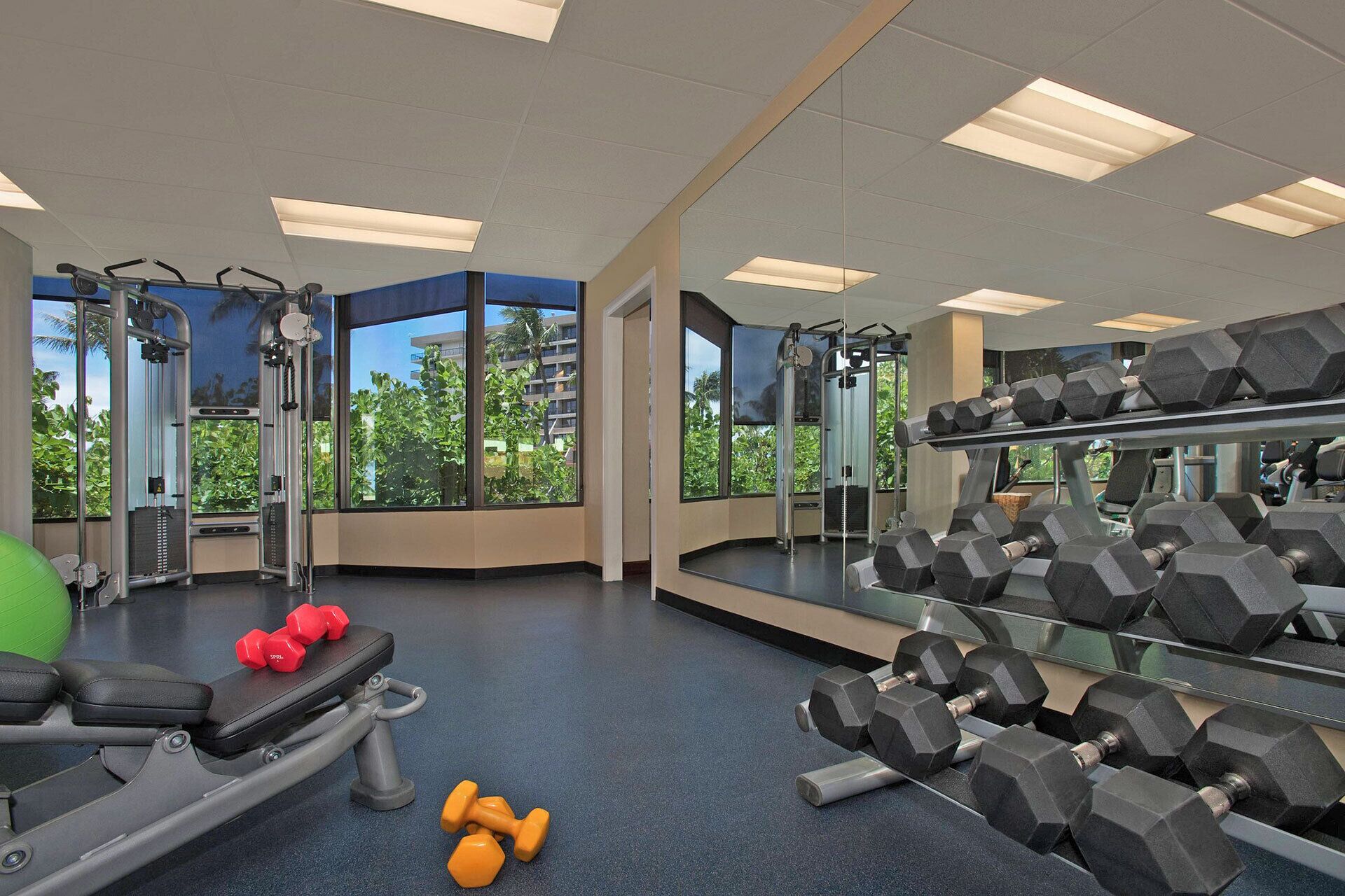 Un gimnasio con equipo de ejercicio, ventanas amplias y un espejo.