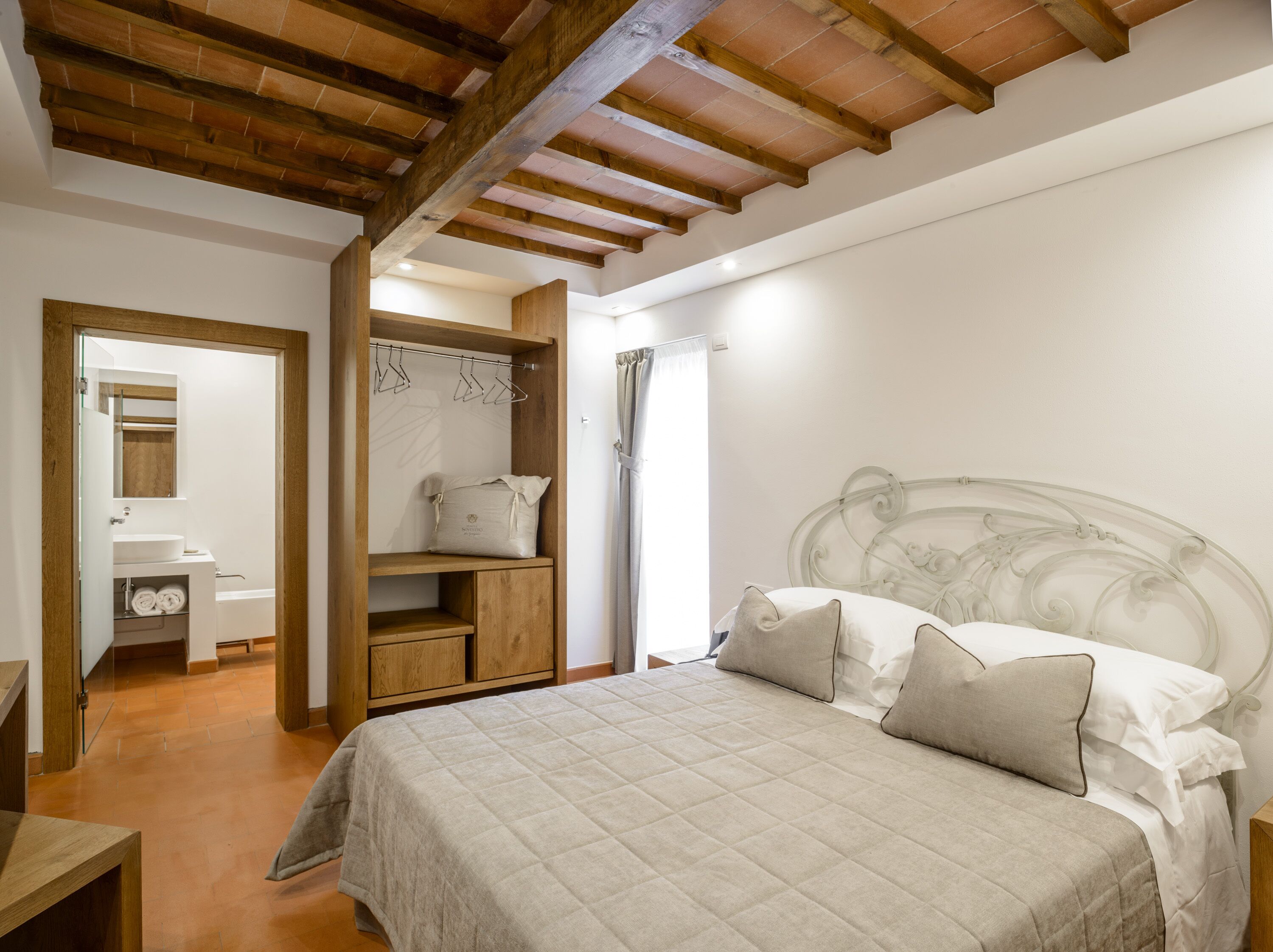 A bedroom with a bed, wooden wardrobe, and a bathroom with a sink and mirror.