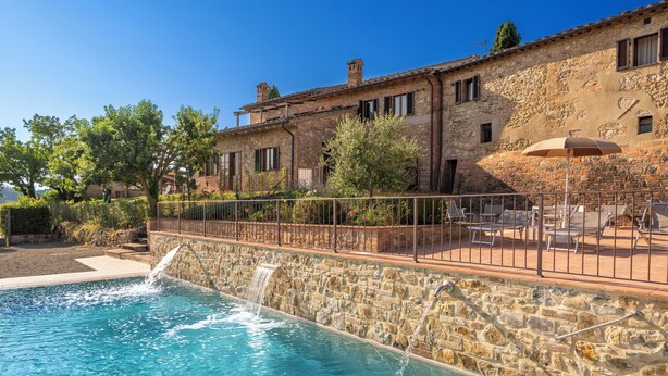 Edificio de piedra con piscina, mobiliario exterior y una cascada.