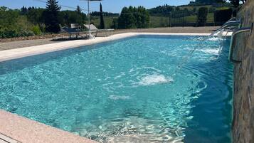 Una piscina limpida con bordo piastrellato, una sedia a sdraio e un ombrellone.