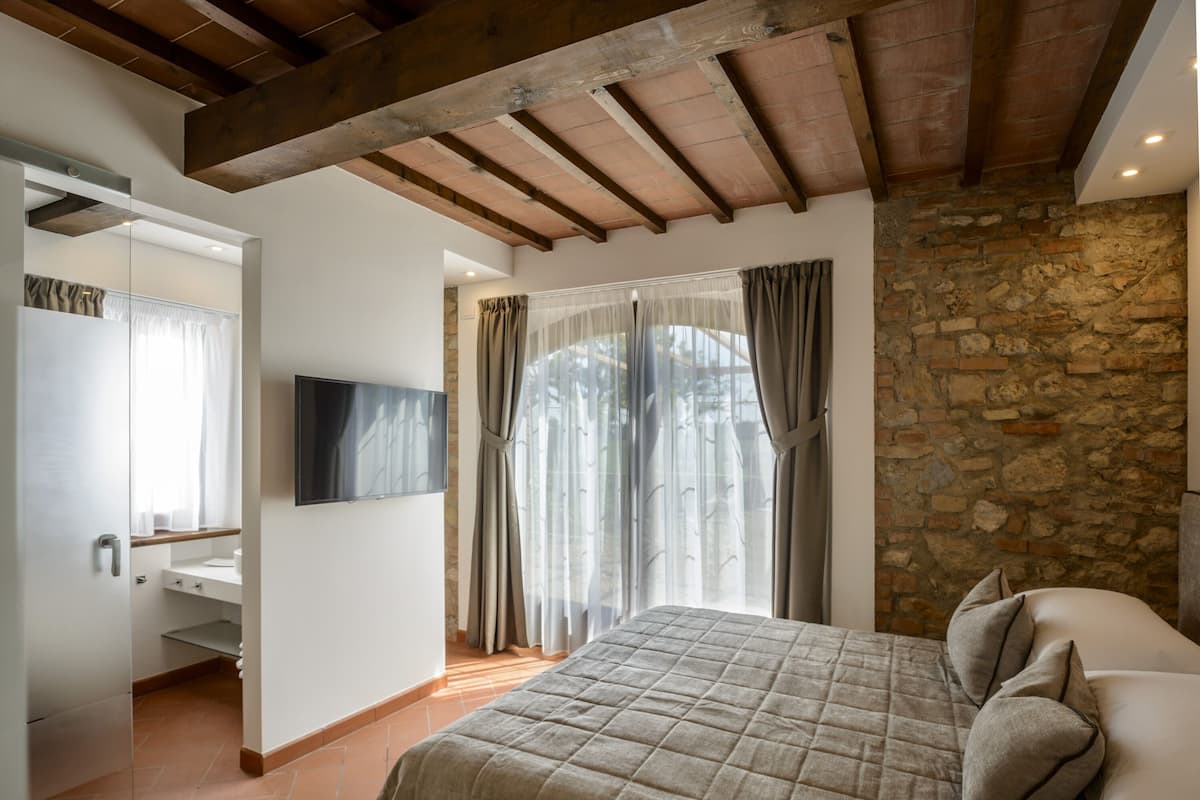 A bedroom with a bed, a TV, a stone wall, and a wooden ceiling.