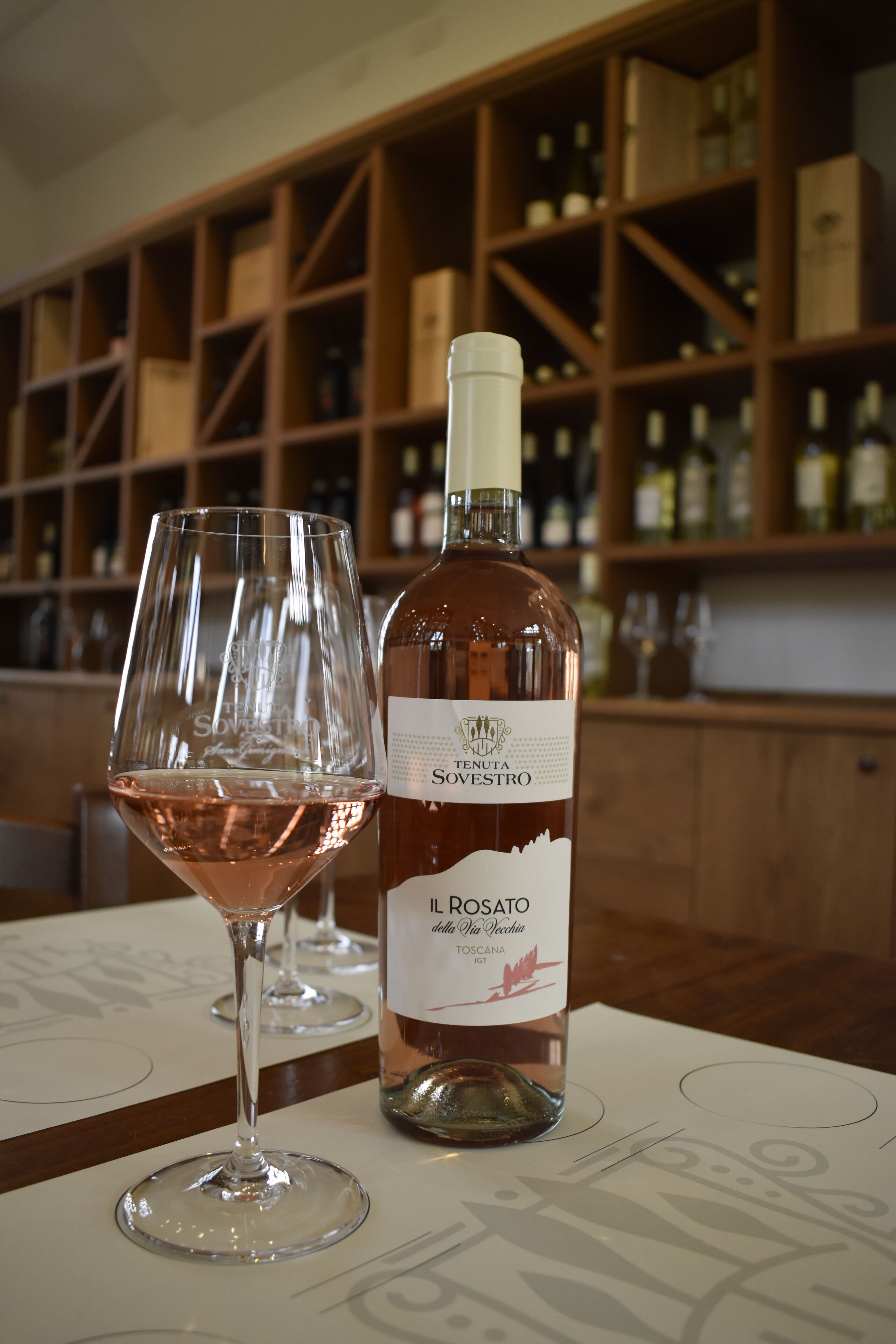 A bottle of Il Rosato Toscana IGT wine and a glass filled with the same wine on a table in a bar setting.
