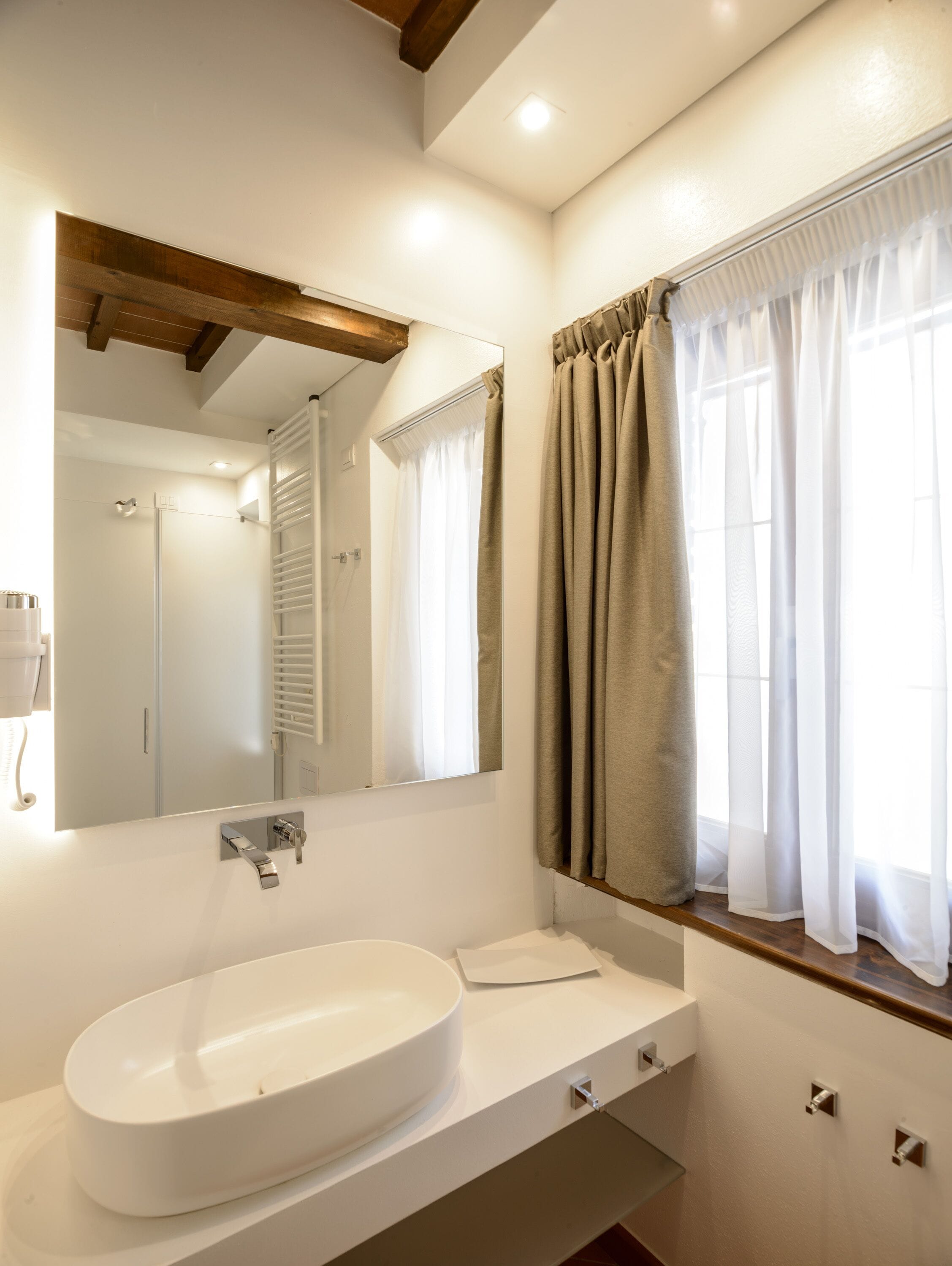 Un baño con lavamanos blanco, espejo y ventana con cortinas.