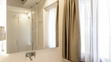 Un baño con lavamanos blanco, espejo y ventana con cortinas.