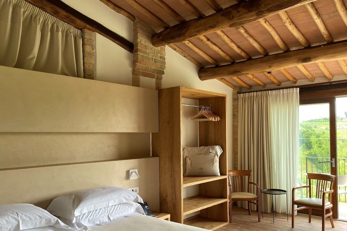 A bedroom with a wooden headboard, a bed with white linens, a wooden wardrobe, and a balcony with a view.