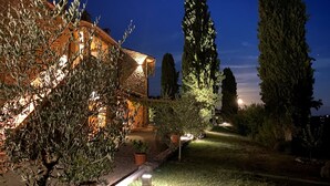 Un espacio exterior bien iluminado con un edificio de piedra, altos árboles y un camino que lleva a la entrada.