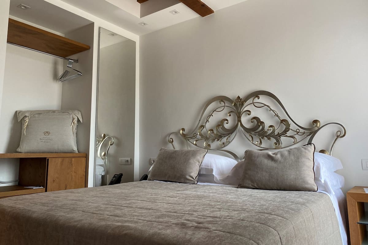 A bedroom with a bed, a wooden shelf, a mirror, and a bedside table.