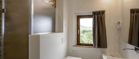 A bathroom with a shower, toilet, and sink, a window with curtains, and a stone wall.