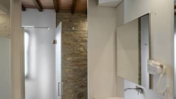 Une salle de bain avec un mur en pierre, un lavabo blanc, un miroir et une douche.