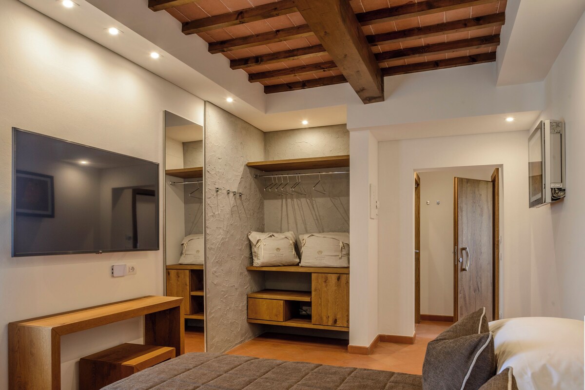 A bedroom with a bed, a wooden bench, a wardrobe, a mirror, and a television.
