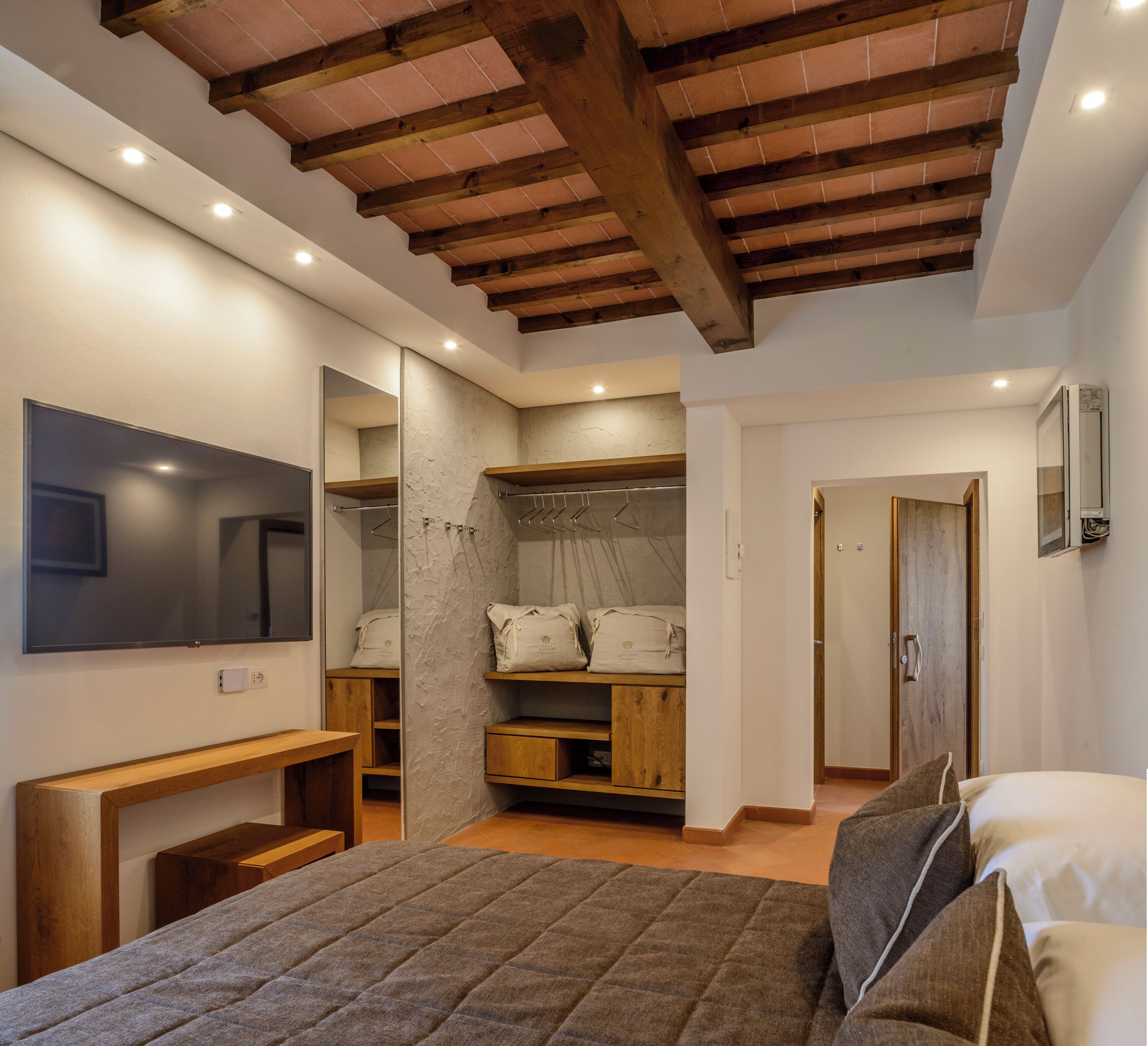 A bedroom with a bed, a wooden bench, a wardrobe, a mirror, and a television.