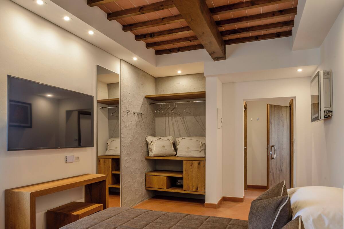 A bedroom with a bed, a wooden bench, a wardrobe, a mirror, and a television.