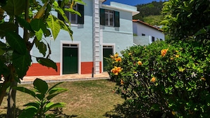 A two-story building with a red and white facade, a white staircase, and a garden with yellow flowers.