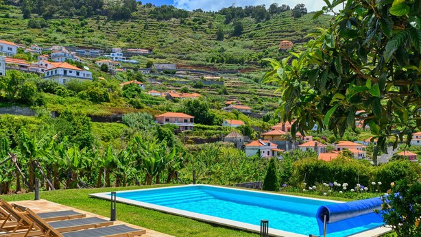 A swimming pool with lounge chairs, surrounded by lush greenery and houses on a hillside.