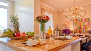 A kitchen with a wooden countertop, a fruit bowl, a vase with flowers, and a colorful crochet wall hanging.