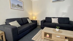 A living room with two black sofas, a wooden coffee table, a lamp, and a framed picture on the wall. - Caboolture, Central Location, Sleeps 6 (Caboolture South)