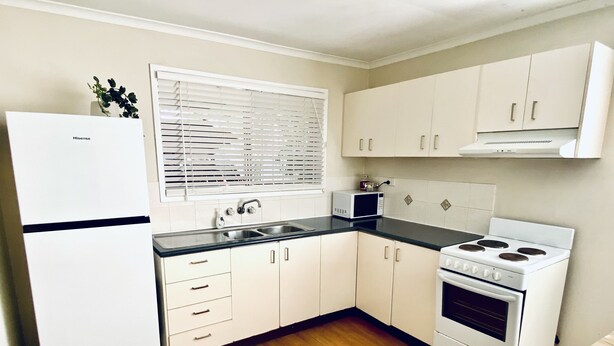 A compact kitchen with white cabinets, a microwave, a stove, and a sink. - Caboolture, Central Location, Sleeps 6 (Caboolture South)