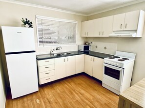 A compact kitchen with white cabinets, a microwave, a stove, and a sink. - Caboolture, Central Location, Sleeps 6 (Caboolture South)