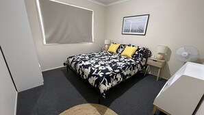 A bedroom with a bed, bedside tables, a lamp, a fan, a picture on the wall, and a window with blinds. - Caboolture, Central Location, Sleeps 6 (Caboolture South)