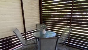 A glass table with four chairs and a vase of flowers, set against a backdrop of horizontal blinds. - Caboolture, Central Location, Sleeps 6 (Caboolture South)